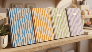 Four colorful diaries with striped patterns on a wooden surface.