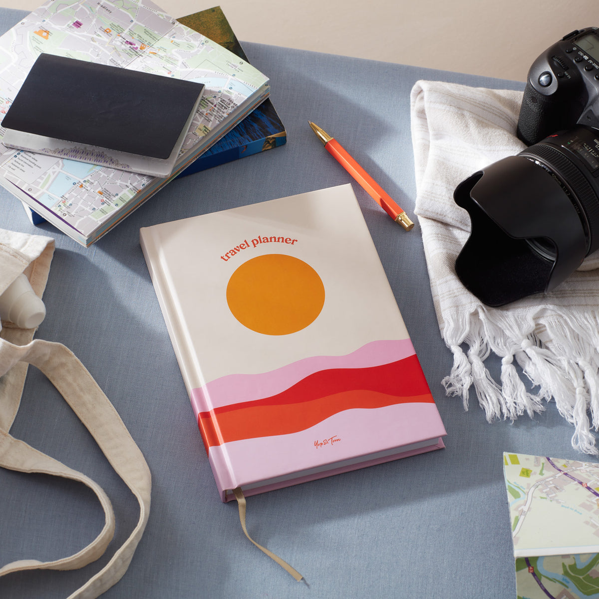 Travel planner with sunset design on a desk surrounded by maps and a camera.