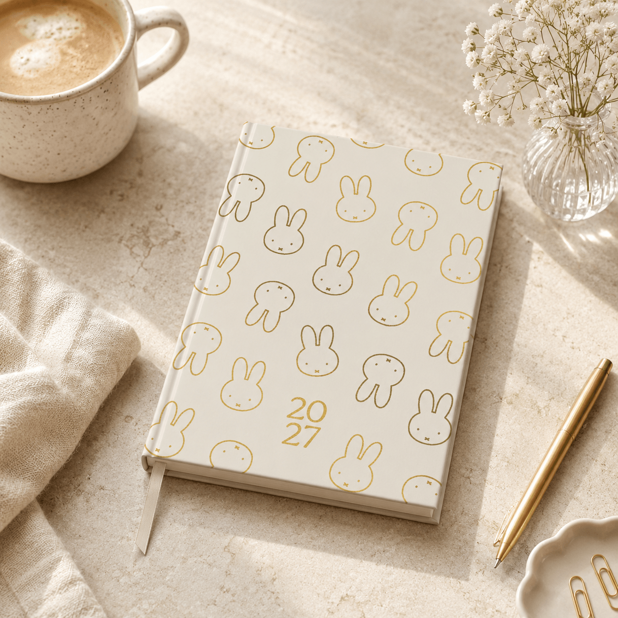Notebook with Miffy bunny pattern and year '2027' on a table with a cup of coffee and pen.