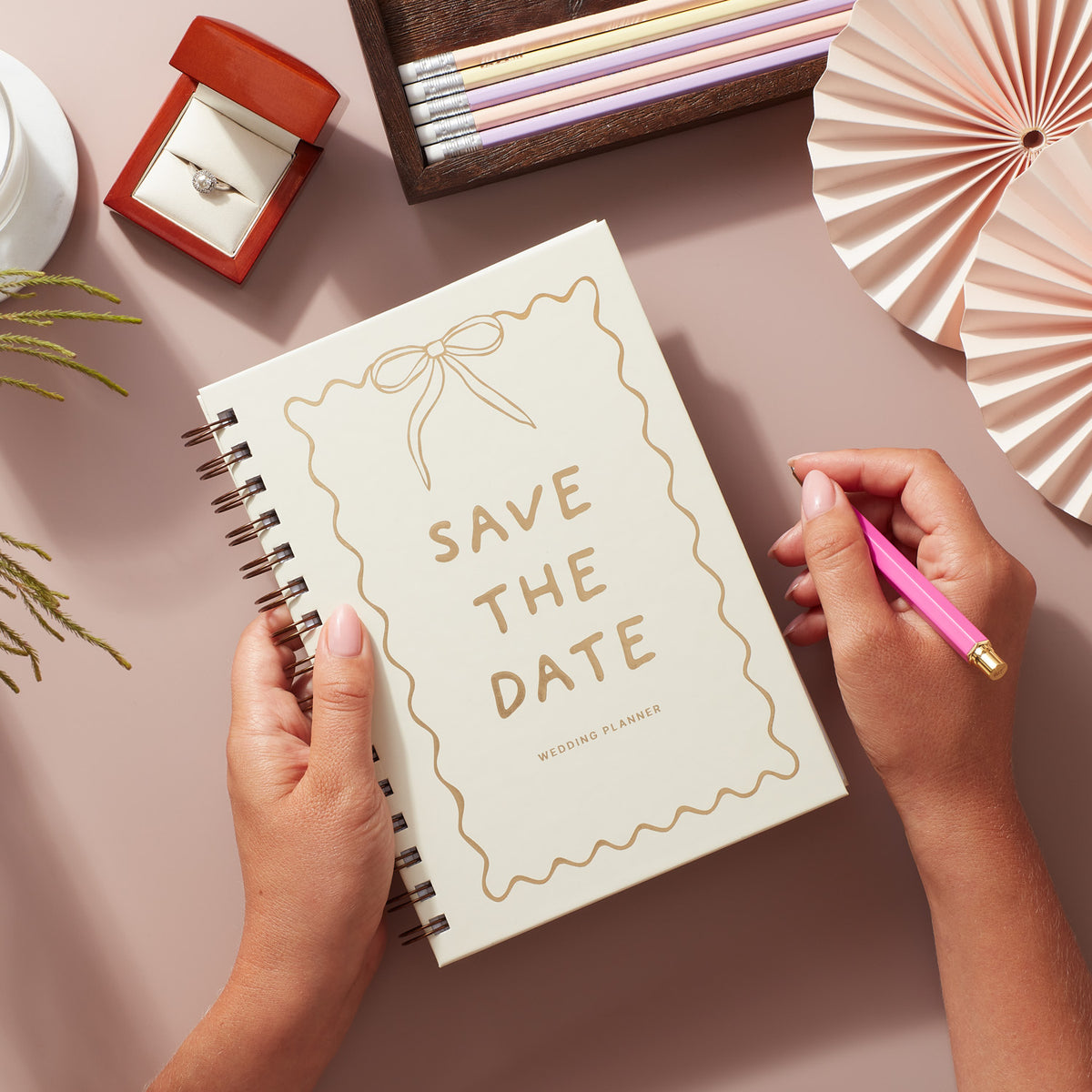 Wedding planner book featuring a Save the Date motif in soft pastels and gold foiling, with a hand holding a pink pen.