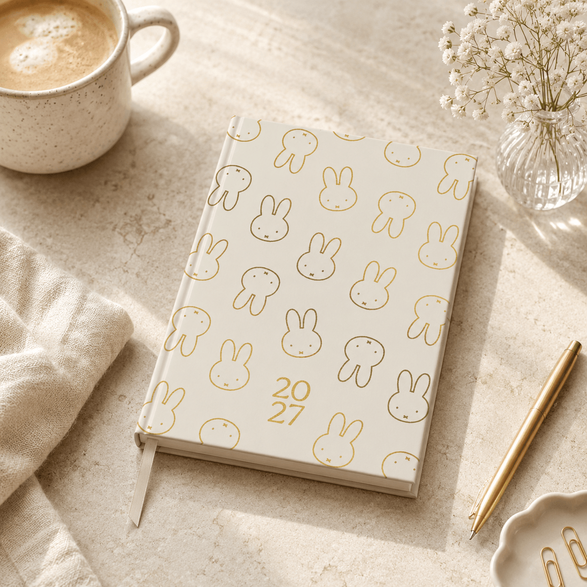 Notebook with Miffy bunny pattern and year '2027' on a table with a cup of coffee and pen.