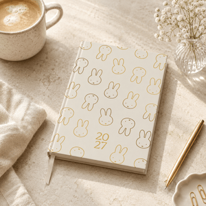 Notebook with Miffy bunny pattern and year '2027' on a table with a cup of coffee and pen.
