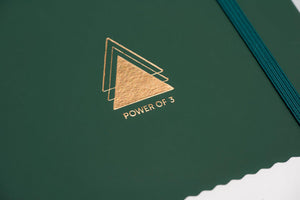 Close up of Power of 3 goal planner gold emblem on forest green cover